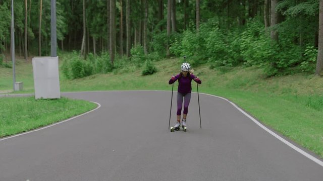 TRACKING Caucasian female professional biathlete roller skiing uphill on a forest track during mid-season practice in summer. ARRI Alexa Mini with Cooke S4 prime lenses RAW graded footage