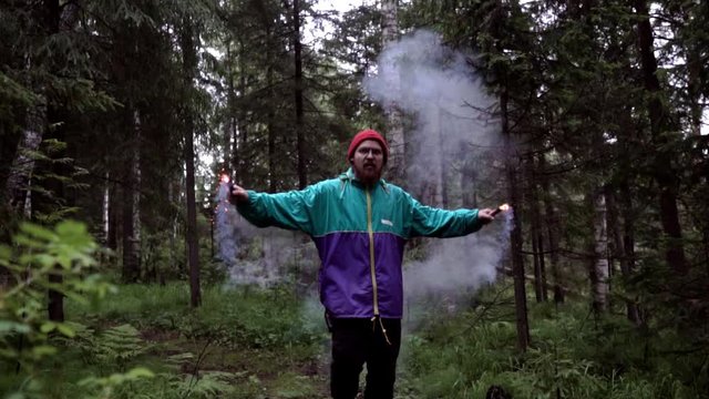 Man and colored smoke bombs in forest. Stock footage. Young man lit smoke colored checkers in forest for beautiful photography
