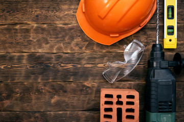 Construction concept background with a copy space. Hardhat, brick, hammer drill and a bubble level on a brown wooden workench.