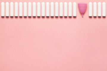Reusable silicone menstrual cup and heap of tampons comparison on a soft pink background. Modern female intimate alternative gynecological hygiene. Eco zero waste concept. Copy space place for text