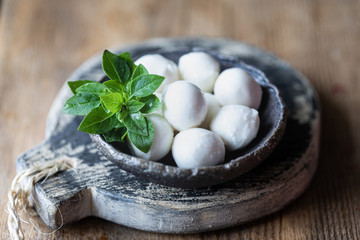 Mozzarella cheese, basil in a ceramic bowl on a wooden board.
