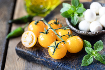 Mozzarella cheese, yellow tomatoes and basil in a ceramic bowl on a wooden board. Olive oil. Caprese salad ingredients. Selective focus