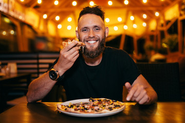 Happy hungry man eating pizza in a bar.