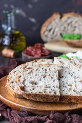 Round loaf of freshly backed sourdough bread with ricotta cheese, dried tomatoes, basil and olive oil. Dark wooden background, rustic style. 