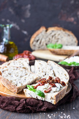 Bread slices with ricotta cheese, sun dried tomatoes and basil served on wooden cutting board. Bruschetta with ricotta cheese, dried tomatoes and basil. 