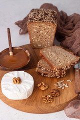 Sliced rye bread on cutting board with camembert cheese and honey. Whole grain rye bread with seeds. Breakfast.