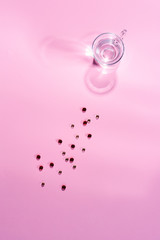 Glass cup with clear water and gelatin capsules on a pink surface. Top view.