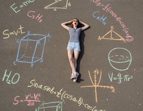 schoolgirl laying on a asphalt with chalk drawn mathenatics formulas and geometric figures