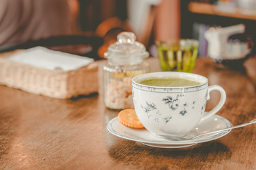 Fototapeta na wymiar green tea matcha soy latte in a china cup with brown sugar and a glass of water on the side