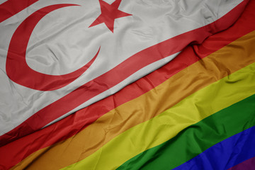 waving colorful gay rainbow flag and national flag of northern cyprus.