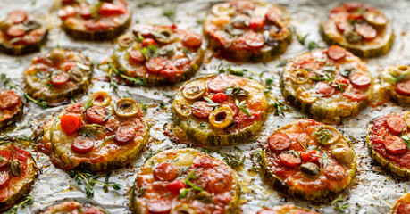 Grilled zucchini slices with addition of mozzarella cheese, sausage, green olives, capers and herbs on white baking paper, close-up. Delicious appetizer, zucchini pizza bites