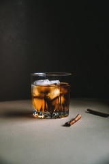 Whiskey with ice cubes and cinnamon stick on dark background. Autumn alcohol concept
