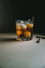 Whiskey with ice cubes and cinnamon stick on dark background. Autumn alcohol concept