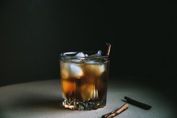 Whiskey with ice cubes and cinnamon stick on dark background. Autumn alcohol concept
