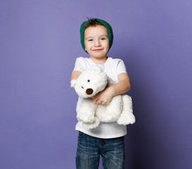 Cute smiling little kid boy in green hat holding hugging his best friend polar bear toy....