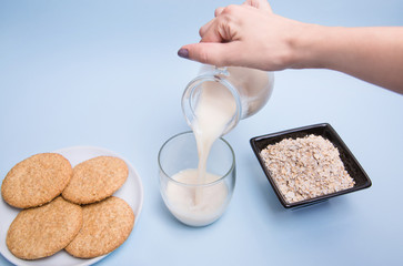 Leche de avena vegana servida en un vaso de cristal sobre una mesa con un bol con copos de avena y un plato de galletas.