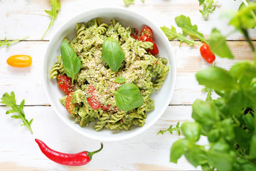 Pasta with green pesto and cherry tomatoes. A dish on a white wooden table