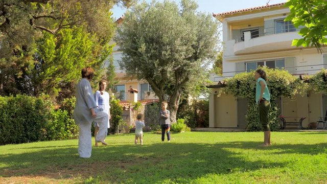 Strengthening soul and body. Exercises in the garden. Happy family having fun while doing sports in slow motion. Children with parents doing exercises on green grass. Vacation on villa in Europe
