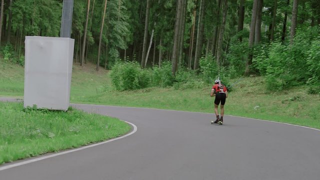 TRACKING Caucasian male professional biathlete roller skiing downhill on a forest track during mid-season practice in summer. ARRI Alexa Mini with Cooke S4 prime lenses RAW graded footage