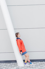 A short haired woman in coral windbreaker and colorful socks staying on road near grey wall © Bohdan Melnyk