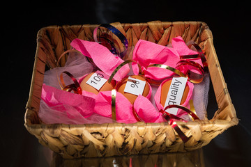 Wrapped in pink paper with different color bow (red, blue, gold)  three eggs are in the wicker basket on the black reflection background/table.  World Quality Day.