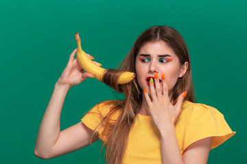 Fototapeta premium Portrait of beautiful young woman with bright color make-up jokingly curling hair with banana.