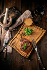Grilled ribeye beef steak with wine, knife and fork on a wooden Board. Whole roast piece of meat, top view and rustic style