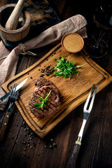 Grilled ribeye beef steak with wine, knife and fork on a wooden Board. Whole roast piece of meat, rustic style