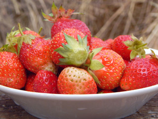 Ripe juicy strawberries in a plate, hay in the background. Farm products, healthy food.