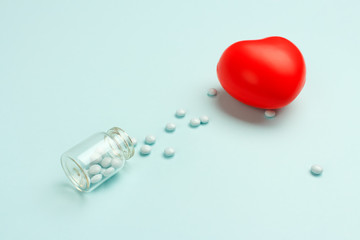 Pills in a glass bottle on a turquoise  background. Drug therapy for the treatment of heart and cardiovascular diseases. Selective focus.