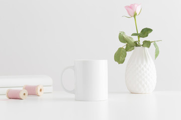 Mug mockup with a pink rose and books on a white table.