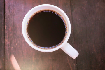 a white mugh of hot black coffee serving on woodentable in morning sunlight