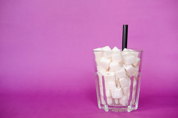 Glass full of sugar cubes  on purple background. Diabetes, sugar disease, unhealthy food, diet concept. Copy space