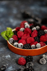 I put it on a dish with a brown rim of berries. Blueberries, raspberries, blackberries lie next to each other, with mint leaves on a dark background.