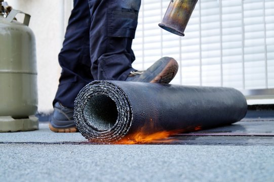 Flat roof installation with propane blowtorch during construction works with roofing felt. Heating and melting bitumen roofing felt. Roofing felt. Roofer working. Roofer working tool. Waterproofing