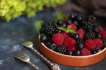 I put it on a dish with a brown rim of berries. Blueberries, raspberries, blackberries lie next to each other, with mint leaves on a dark background.