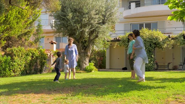 Three generations having fun while doing exercises on green grass in the garden. Adults and children care about their health. Doing yoga fitness exercises on the villa near the sea. Slow motion
