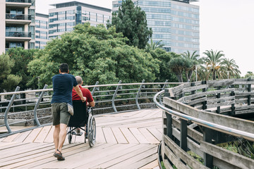 Fototapeta na wymiar man pushes his friend's wheelchair into the park