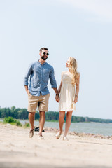 adult happy couple walking along beach and holding hands