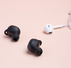 black wireless and white earphones with wire on a beige background