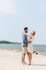 side view of happy blonde woman hugging bearded boyfriend at beach