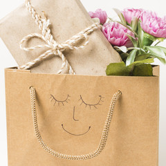 Close-up of flower bouquet and wrapped gift box in paper bag with hand drawn face on it