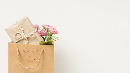Flower bouquet and wrapped gift box in paper bag with hand drawn face isolated on white background
