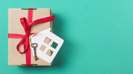 Brown gift box tied with red ribbon; and house key over turquoise surface