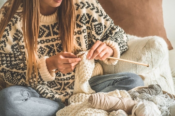  Beautiful girl knits a warm sweater on the bed. Knitting as a hobby. Accessories for knitting.