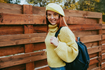 Obraz premium Pretty young red hair ginger hair sweater and yellow beret hat posing in park near wooden wall. Beautiful woman wearing trendy seasonal clothes in autumn.