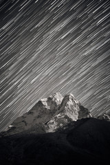 Stars falling above Ama Dablam mountain peak lit up by a bright moonlight. Stars trails above Himalayan mountain range.