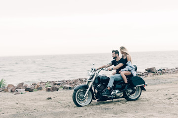 Fototapeta na wymiar young couple of bikers on black motorcycle at beach near river