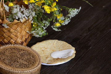 National traditional food for the holiday. Pancakes with sour cream. Wicker basket with flowers stands on a wooden table.