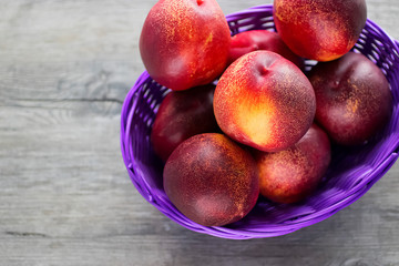Ripe organic nectarines in purple  basket on  gray background.